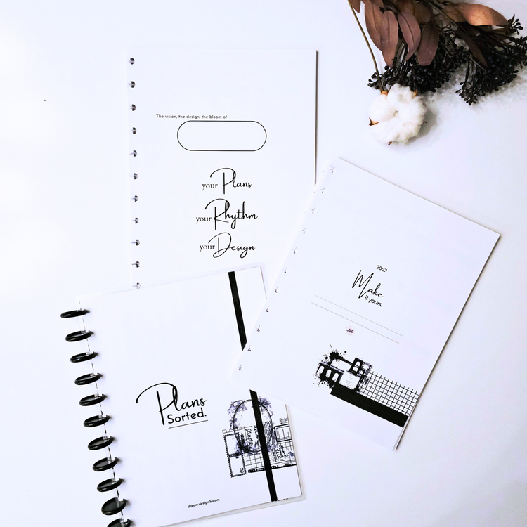 Four dream.design.bloom 2027 discbound planner notebooks with floral and vintage-style covers are arranged on a light surface with a gold pen nearby. The covers show the visible brand text 'Plans Sorted.