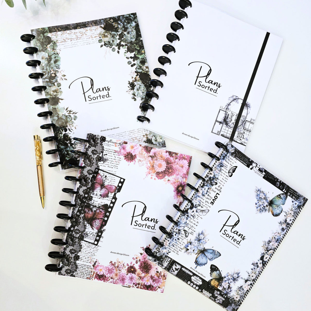 Four dream.design.bloom 2027 discbound planner notebooks with floral and vintage-style covers are arranged on a light surface with a gold pen nearby. The covers show the visible brand text 'Plans Sorted.