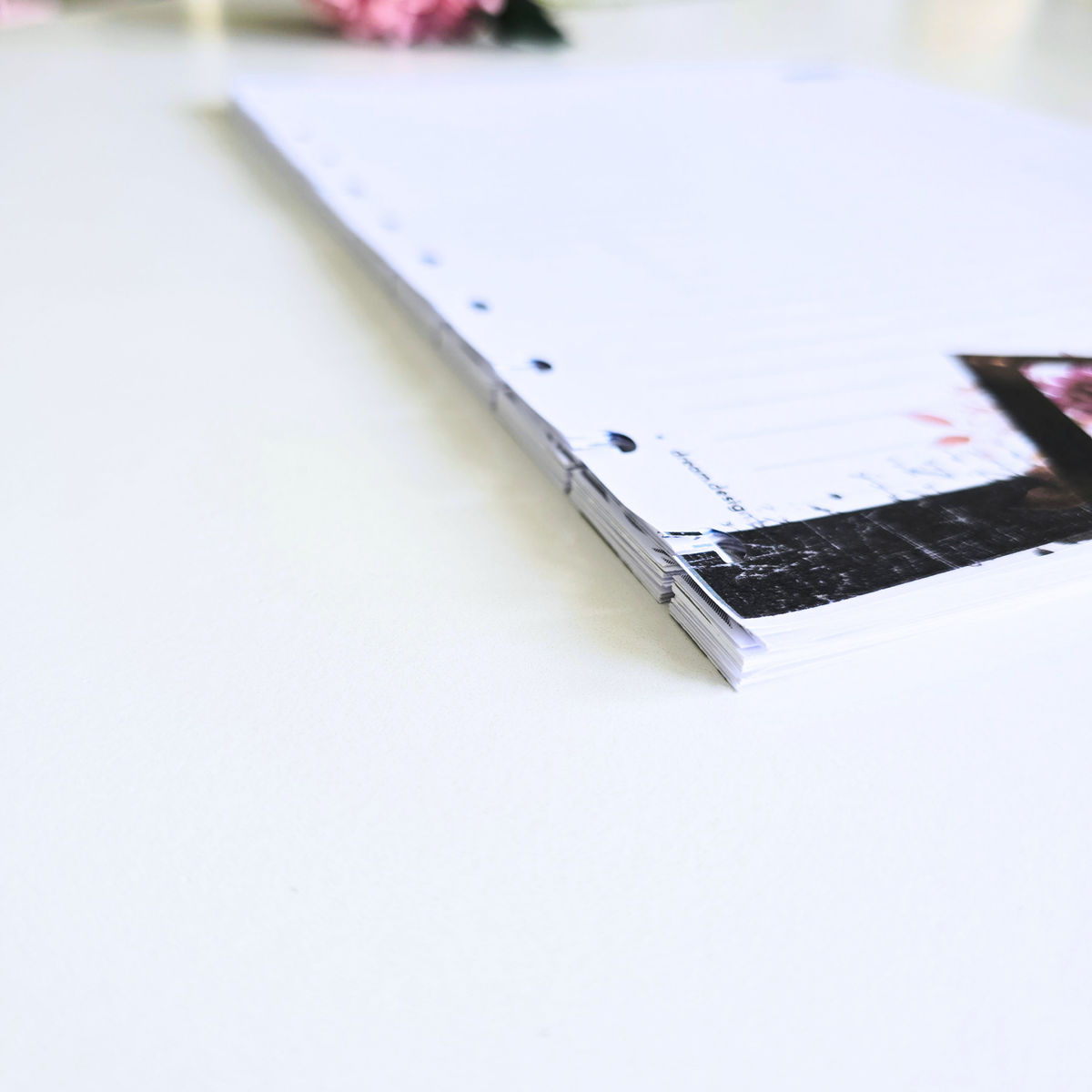 A close-up of discbound notes pages
with lined writing space, shown on a clean white surface. The binding is pale pink, and part of a printed page design with a dark rectangular photo insert is visible.