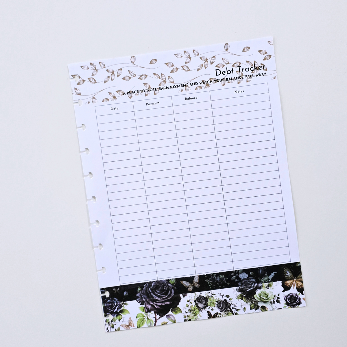 A discbound debt tracker notebook page with lined fields for date, percentage, balance, and notes, decorated with a floral vine border at the top and a black rose pattern at the bottom, shown on a light grey background. Disc Bound Planner