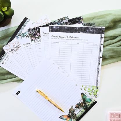 A styled flat-lay of a discbound planner notepad set with various budgeting, shopping, and tracking sheets, featuring a gold pen and a green fabric background. Disc Bound Planner