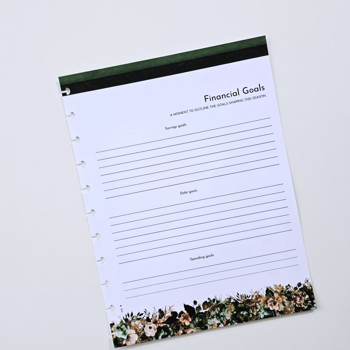 A discbound planner insert page titled 'Financial Goals' with lined writing space, a dark green top border, and a floral border along the bottom, photographed on a light neutral background. Disc Bound Planner. Discbound Inserts
