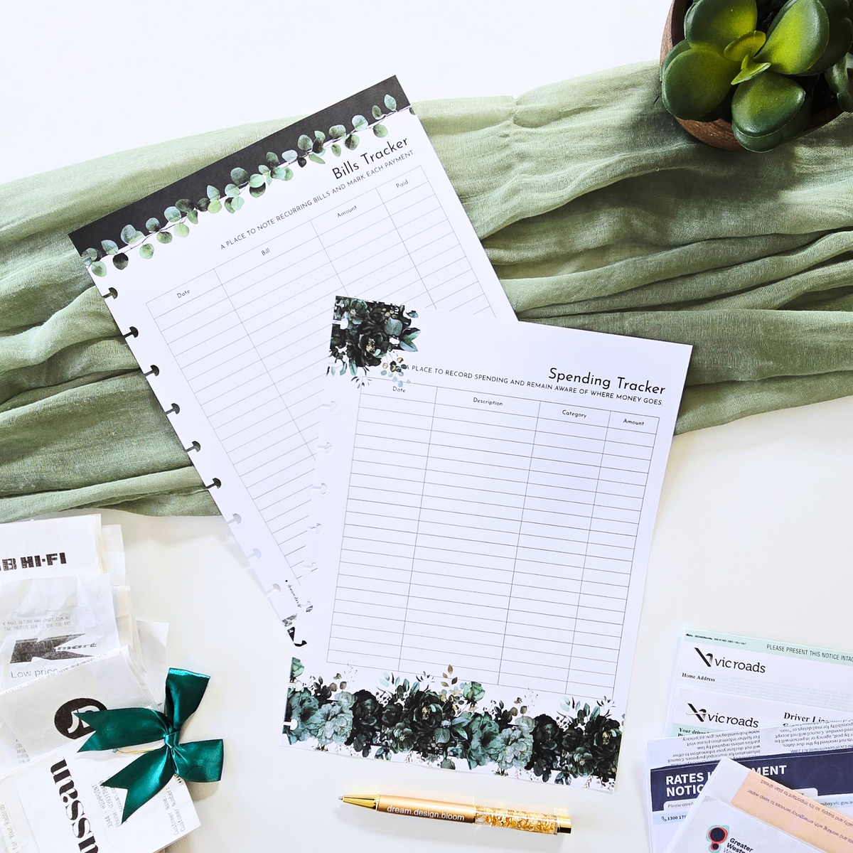 Two disc bound planner inserts, a Bill Tracker and a Spending Tracker, styled on a white surface with a sage green fabric backdrop, a gold pen, and small decorative props. Discbound Planner