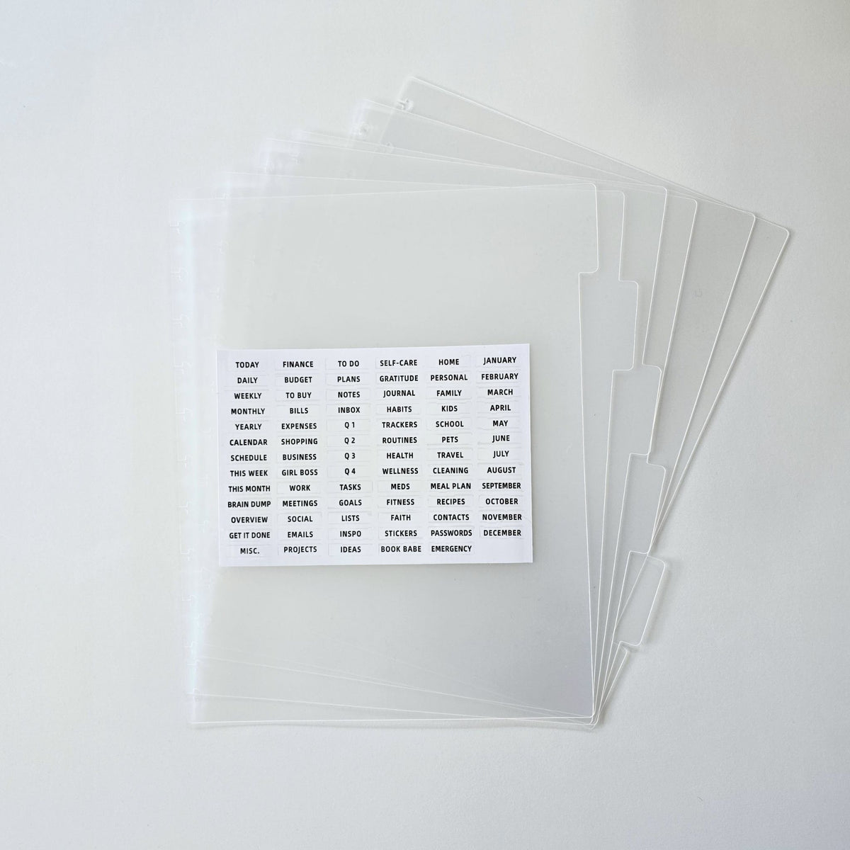 A stack of clear plastic document side tabs for discbound planning with a small white card showing sample printed text, photographed on a clean white background.