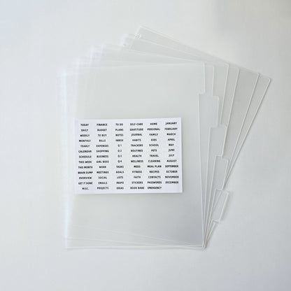 A stack of clear plastic document side tabs for discbound planning with a small white card showing sample printed text, photographed on a clean white background.