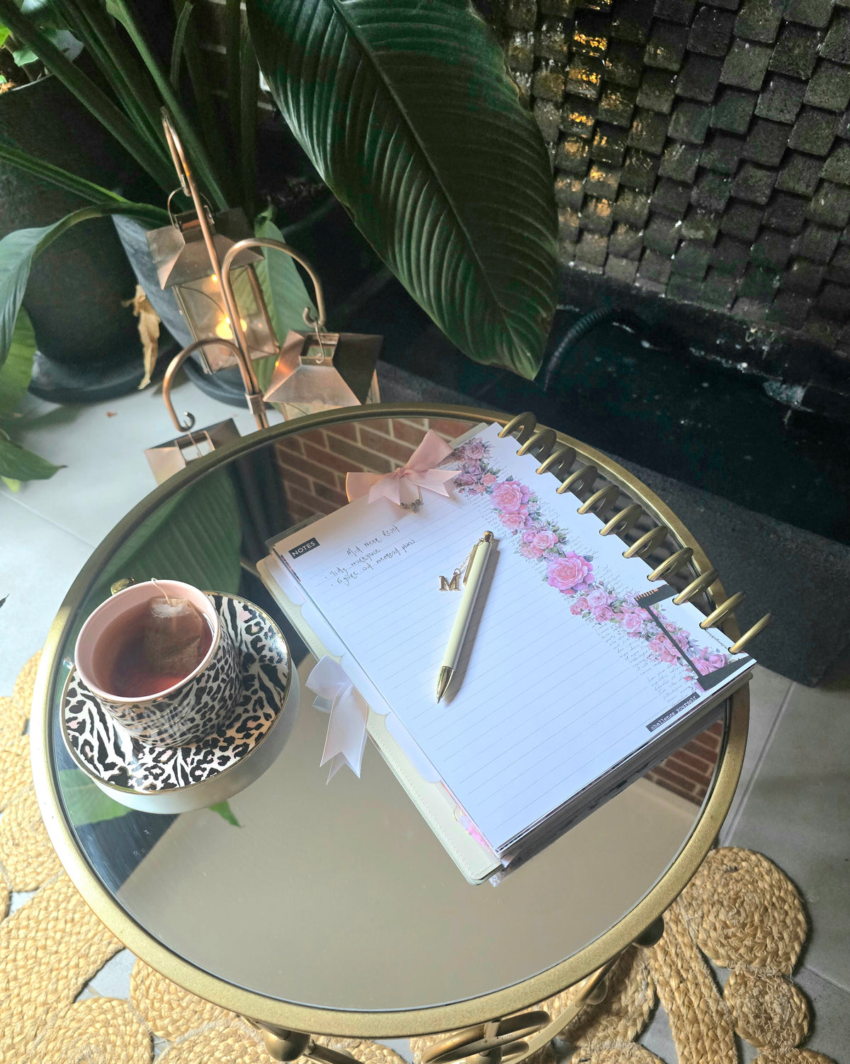 dream.design.bloom discbound planner open to a notes page, placed on a table in front of a gentle indoor fountain surrounded by greenery. A calm Wellness Wednesday scene for restful planning